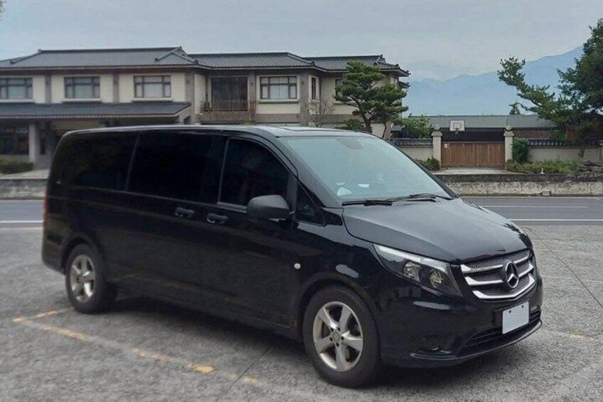A black van parked in a lot with a building and trees in the background. 2