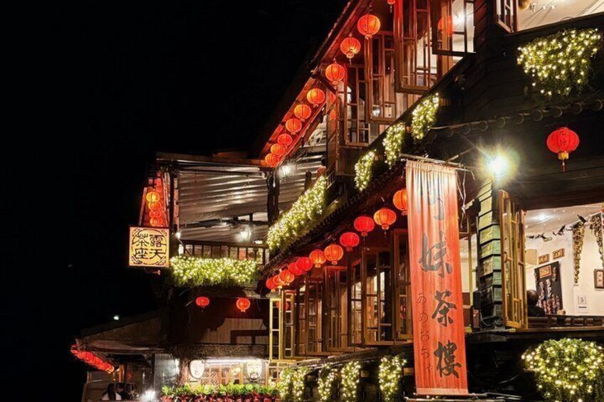 A traditional building with red lanterns and greenery, illuminated at night. 1