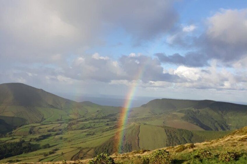 A landscape with rolling hills, a rainbow, and a cloudy sky. 2