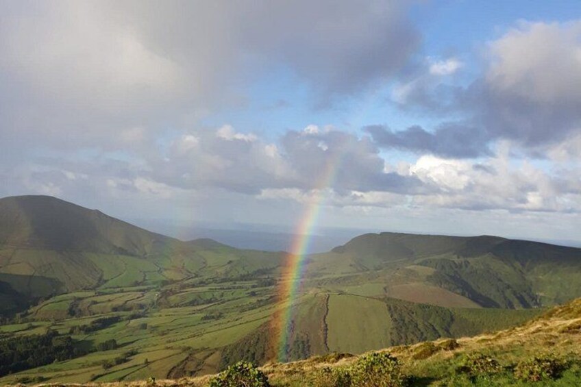 A landscape with rolling hills, a rainbow, and a cloudy sky. 2