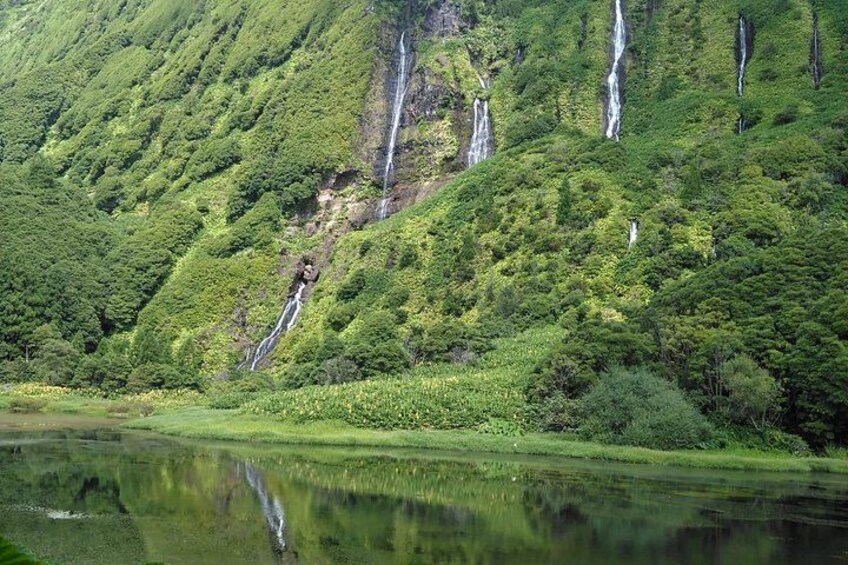 A mountainous landscape with multiple waterfalls cascading down the slopes, surrounded by lush greenery and a calm body of water reflecting the scenery. 5
