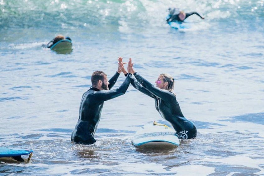 Two people in wetsuits giving each other a high-five in the ocean with surfboards nearby. 4