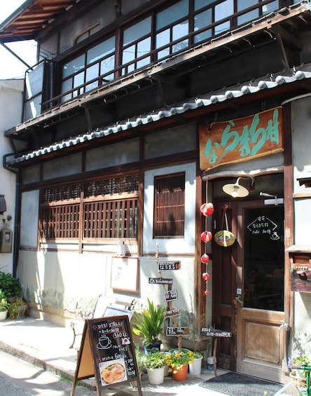 A traditional Japanese building with a signboard, wooden shutters, and a small garden with potted plants. 3