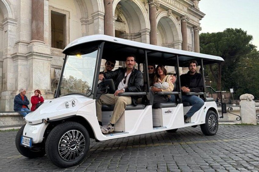 A white golf cart with passengers, parked in front of a classical building with columns. 2