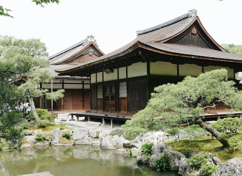 A traditional Japanese building with a pond, surrounded by rocks and trees. 1