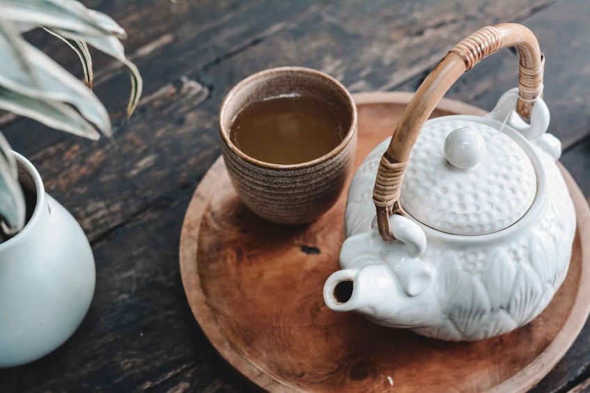 A white teapot with a wooden handle on a wooden tray, accompanied by a brown cup of tea. 2