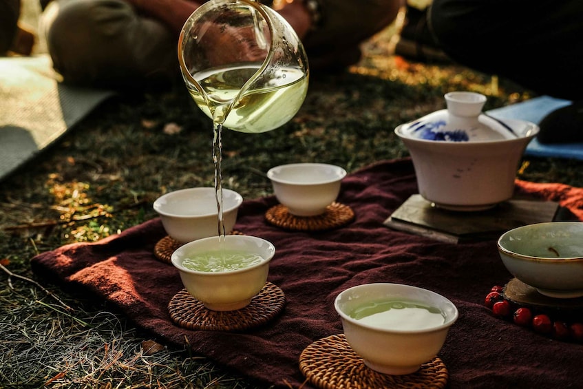 A glass pouring liquid into bowls on a cloth outdoors. 3