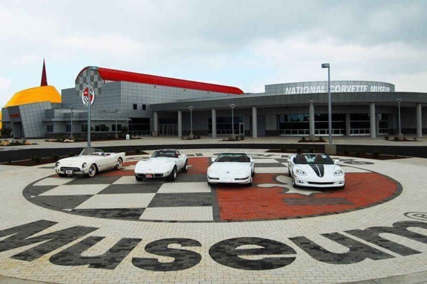 The National Corvette Museum with a checkered floor pattern and several white sports cars parked in front. 1