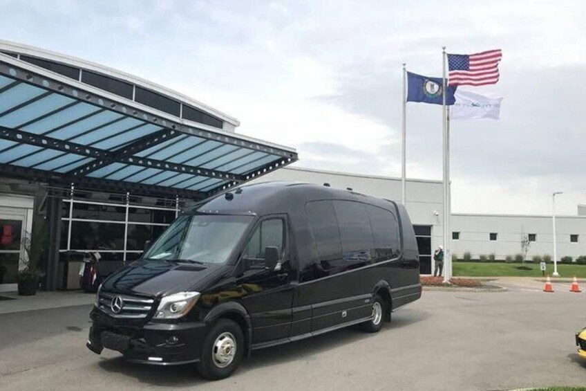 A black Mercedes-Benz van parked in front of a building with a glass roof and two flags, one of which is the American flag. 3