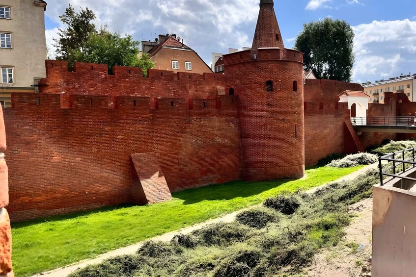 A brick wall with a conical tower, a grassy area, and a paved path. 3