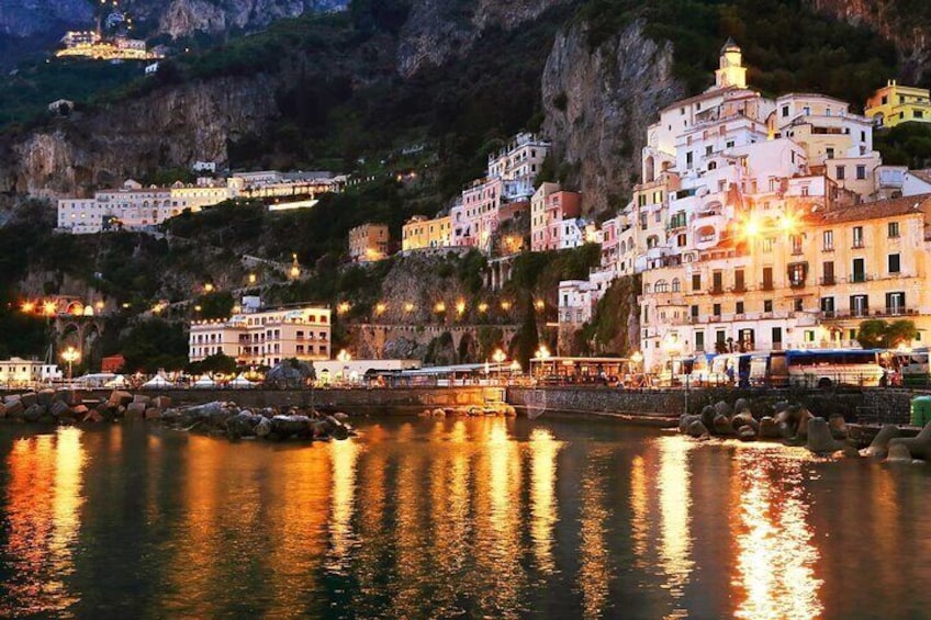 A coastal town at dusk with illuminated buildings reflecting on the water. 4
