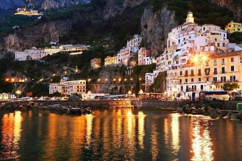 A coastal town with buildings along the water, a bridge, and a rocky hillside. 4