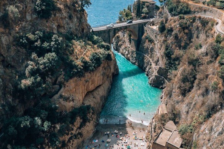A coastal cliff with a bridge, turquoise water, and a beach with people. 3