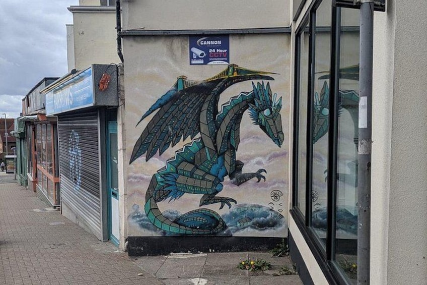 Een muurschildering van een draak op een gebouw, een gesloten winkel met een luik, en een bordje met CANNON erop. 1