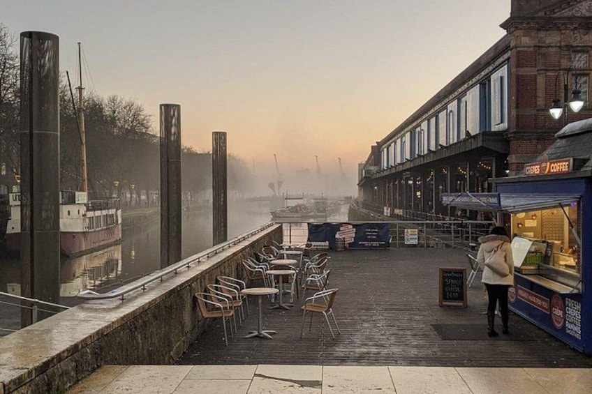 Een café aan het water met tafels en stoelen, een koffieautomaat en een mistige rivier op de achtergrond. 4