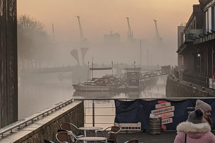Een mistige haven met boten, een steiger en een persoon in een roze jas. 3