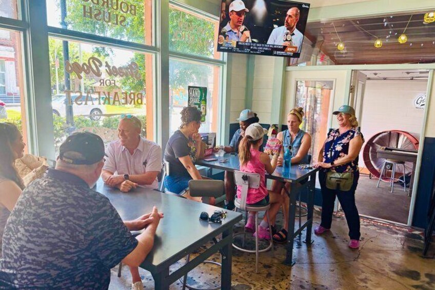 A group of people seated at tables inside a restaurant with large windows and a television mounted on the wall. 5