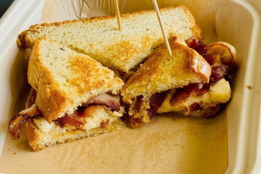 A grilled sandwich with bacon and cheese, cut in half, held together with toothpicks. 1
