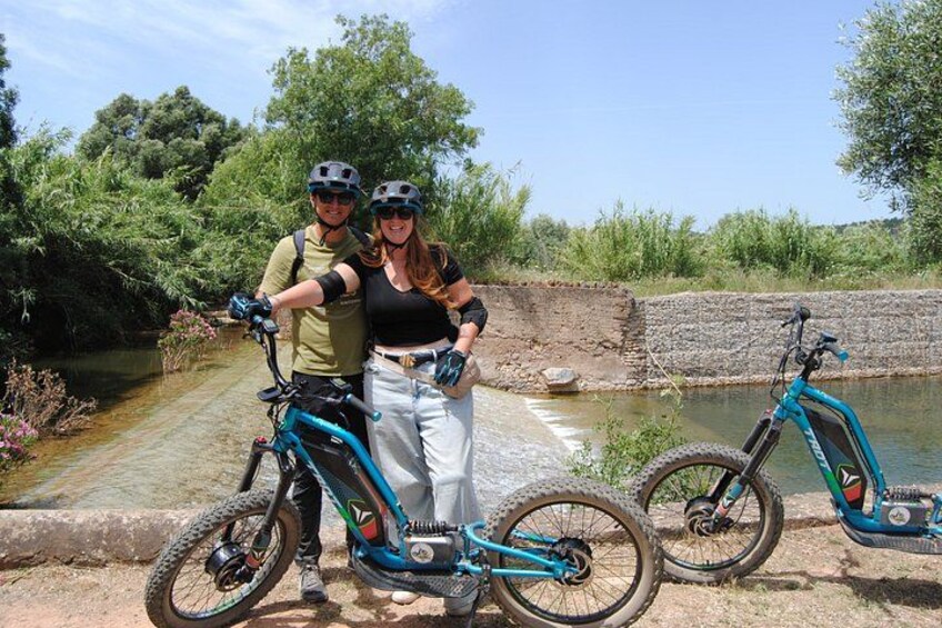 Two people standing by a canal with bicycles. 1