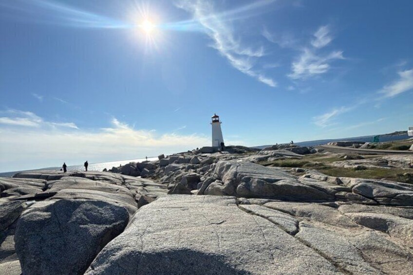 A lighthouse on rocky terrain with the sun shining in the sky. 5