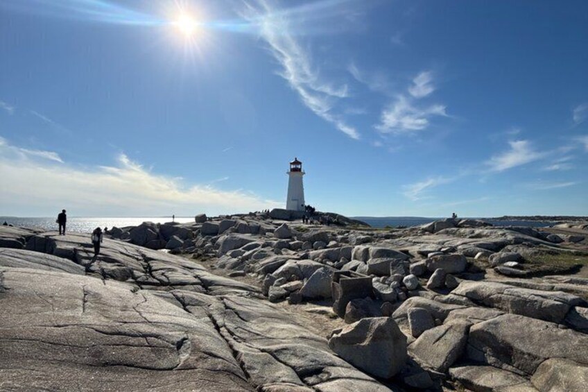 A lighthouse on a rocky shore with people walking nearby. 1
