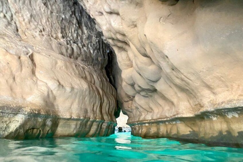 A boat in a turquoise water body with a rocky cave-like formation in the background. 2