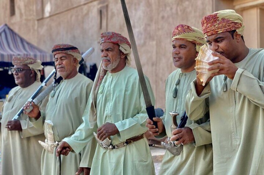 A group of men in traditional attire holding swords and a shell. 5