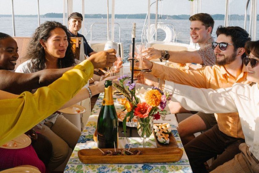 A group of people toasting with champagne on a boat with a floral tablecloth. 2