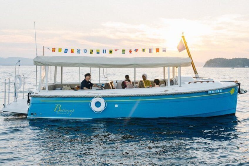 A blue boat with a white canopy and a flag, named 'Buttercup,' on calm water with a sunset in the background. 2