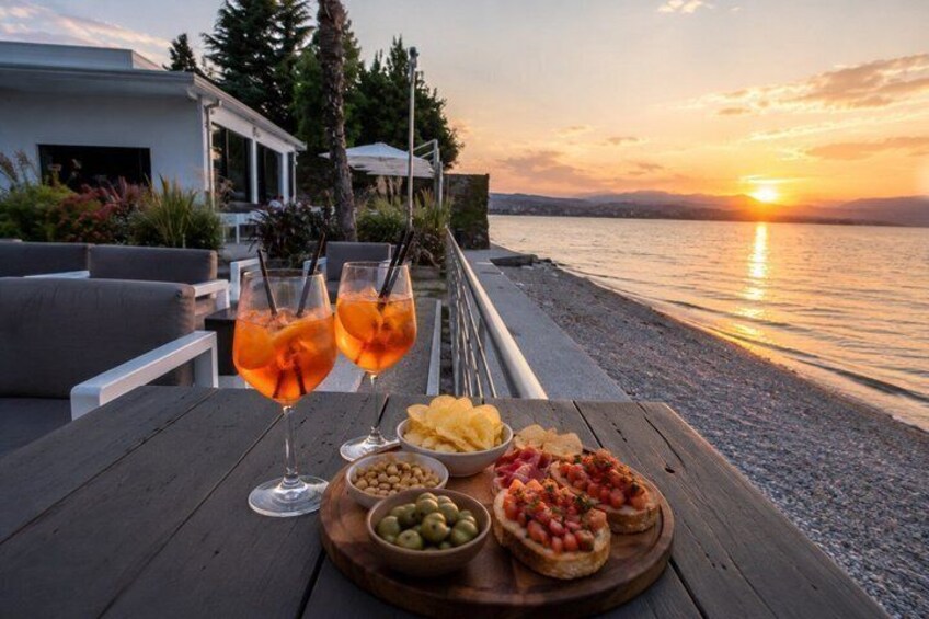 A sunset by the water with a table set for a meal and drinks. 5