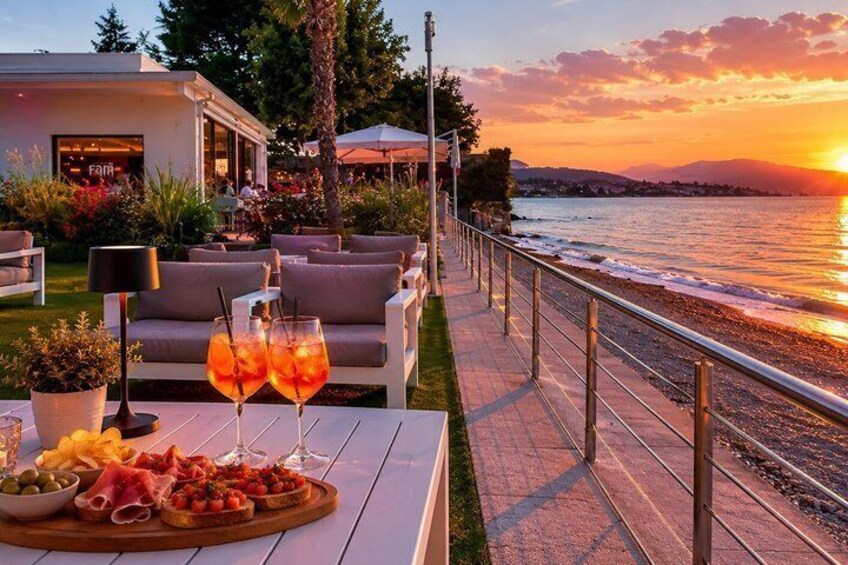A seaside terrace with a sunset view, outdoor seating, and a tray of food and drinks. 4