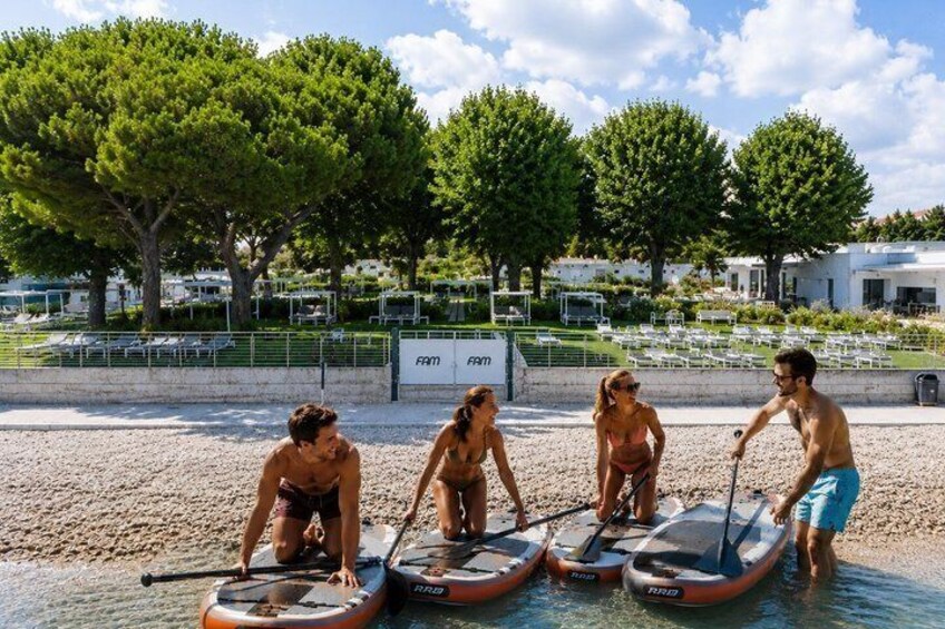 People on paddleboards at a beach with trees and a sign in the background. 1
