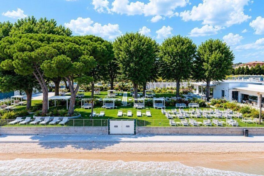 A beachside resort with sun loungers, trees, and a building in the background. 2