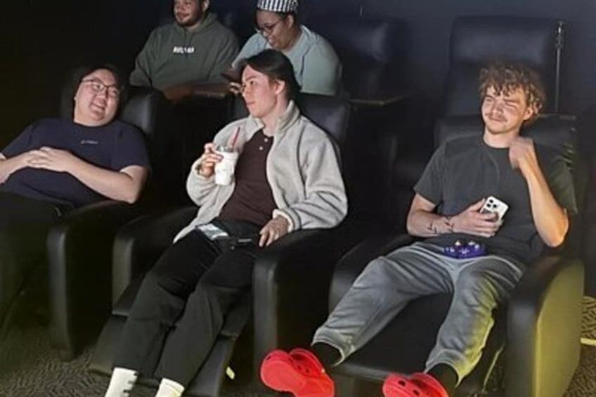 People seated in a row of black chairs, some holding drinks. 2