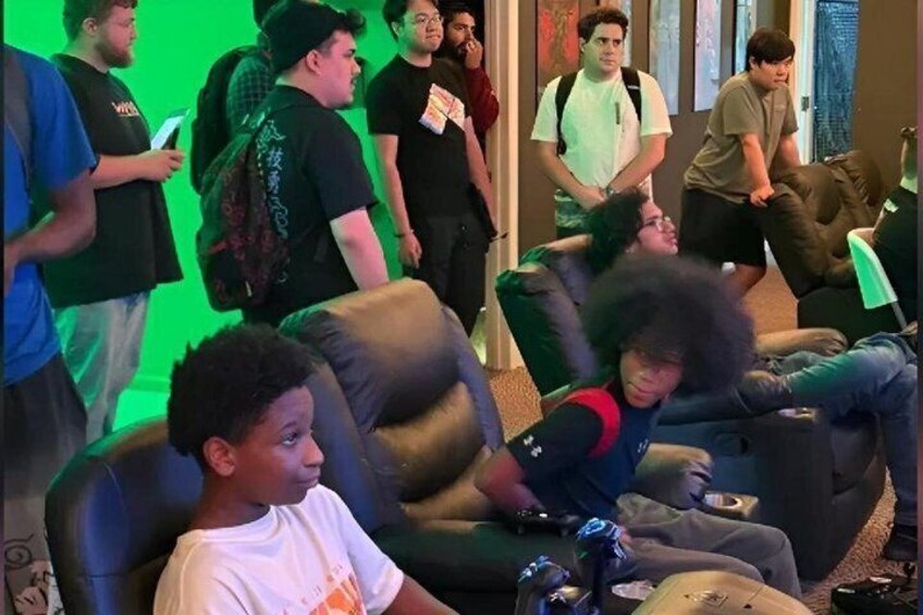 A group of people in a room with green lighting, some sitting on couches and others standing. 4