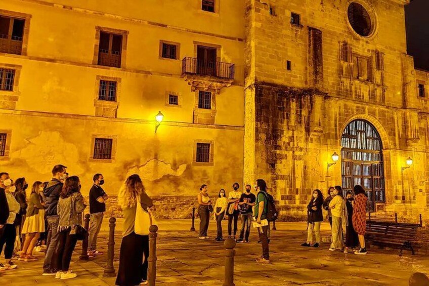 A group of people standing in front of a historic building at night. 2