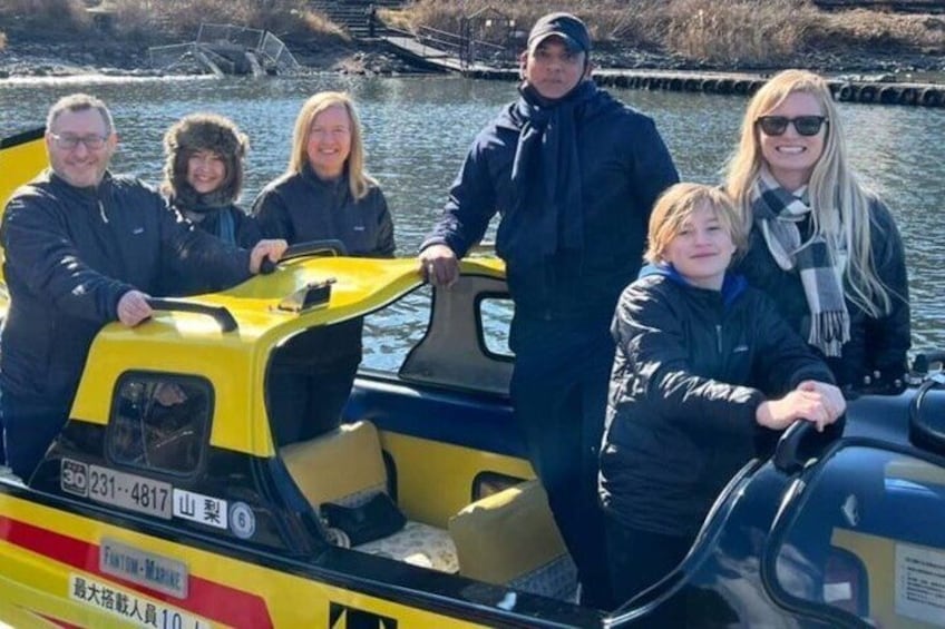 A group of people on a yellow boat with a cabin, a river, and a bridge in the background. 2