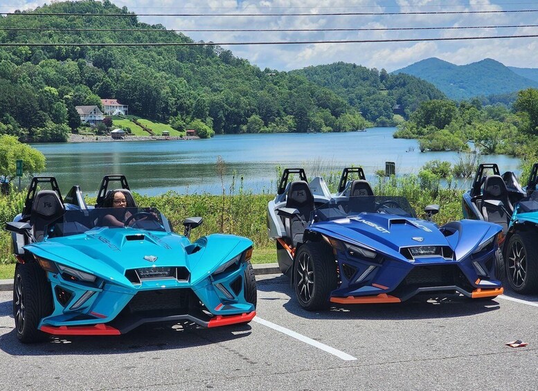 Two sports cars parked in a lot with a lake and mountains in the background. 1