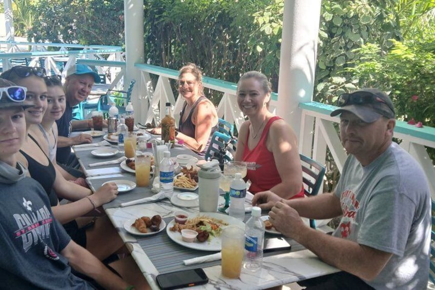 A group of people dining at an outdoor table with food and drinks. 1