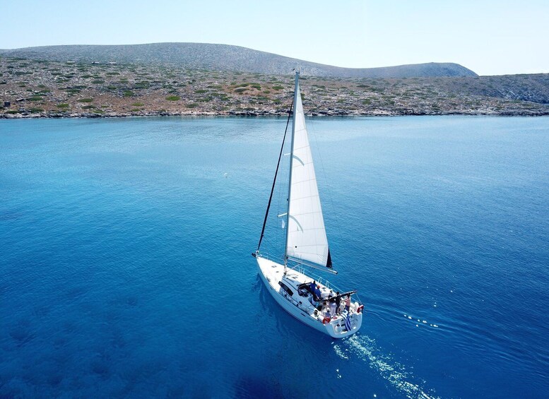 A sailboat on a calm sea with a mountainous coastline in the background. 1