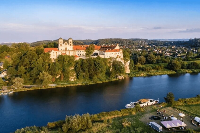 A castle on a hill overlooking a river, surrounded by greenery and a small town. 1