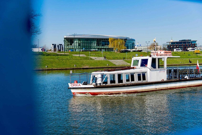 A riverboat named ORKA on calm waters, with modern buildings and a clear sky in the background. 4
