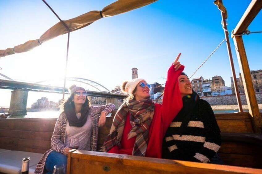 Three people on a wooden boat with a bridge in the background. 5