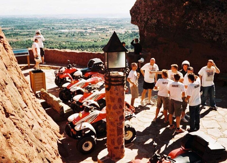 A group of people standing on a stone platform with a view of the landscape, surrounded by red vehicles. 5