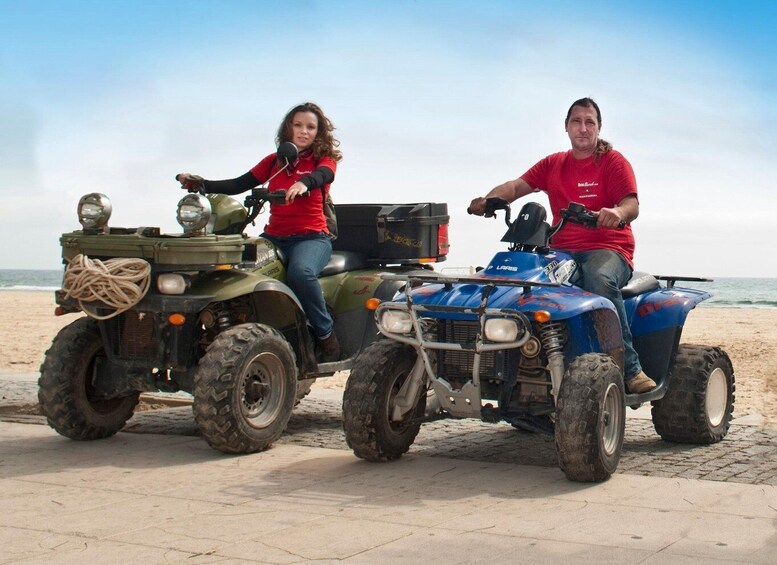 Two people on ATVs on a beach with the ocean in the background. 1