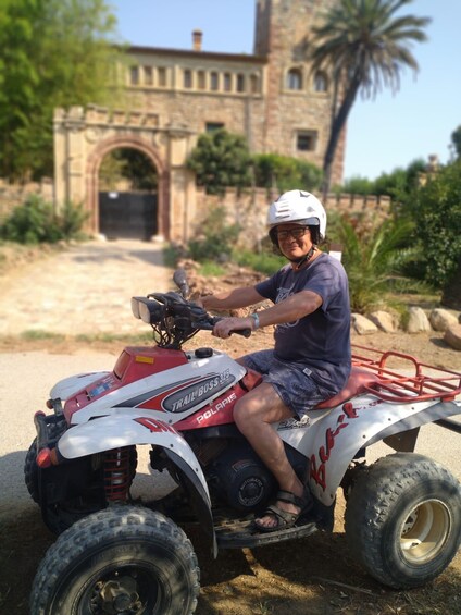 A person riding a red and white ATV on a dirt road with a stone building and palm trees in the background. 2
