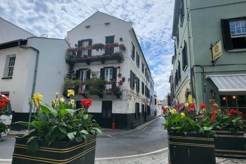 A street with white buildings, flower pots, and a clear sky. 2