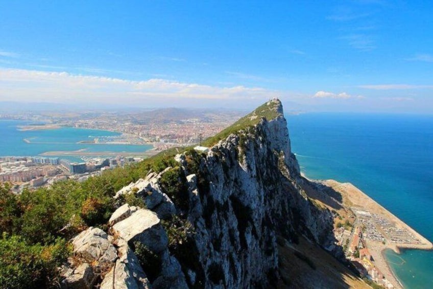 A coastal cliff with a view of the sea and a distant cityscape. 1