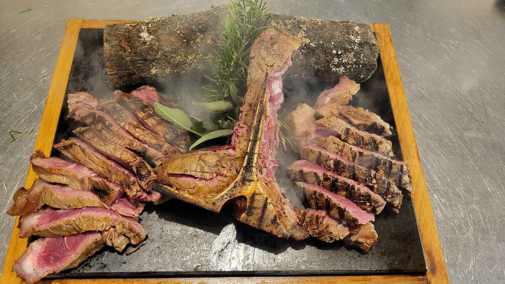 A steak with a bone, sliced and arranged on a black plate, with a sprig of rosemary and a green herb beside it. 5
