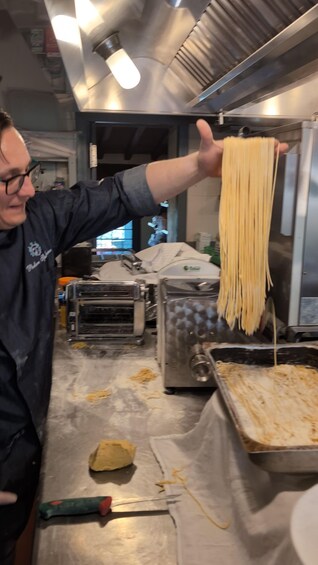 A person holding a long noodle in a kitchen. 4